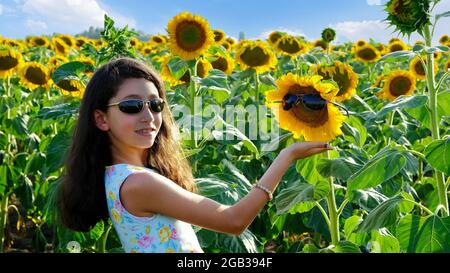 Ein schönes Mädchen grüßt die Sonnenblume und die Sonne. Stockfoto