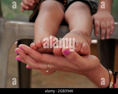 Kleine Kinder Füße auf weibliche Hand gehalten, Pflege Konzept mit Jungen Fuß vorgestellt. Stockfoto