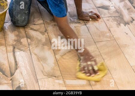 Arbeiter, der die neu verlegte Keramikfliese mit Fugenmaterial bemundet. Bewegungsunschärfe beabsichtigt. Stockfoto