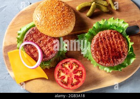 Burger. Hausgemachte Hamburger-Zutaten, amerikanisches Essen. Köstliche Rindersteaks, Salat, Gemüse und Gurken, über dem Kopf flach auf einem Holzbrett Stockfoto