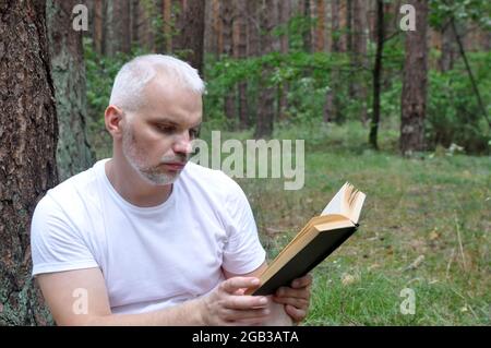 Ein Mann liest im Wald ein Buch und entspannt sich an der frischen Luft. Nahaufnahme. Stockfoto