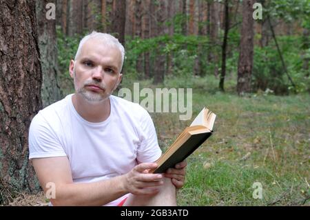 Ein Mann liest im Wald ein Buch und entspannt sich an der frischen Luft. Nahaufnahme. Stockfoto