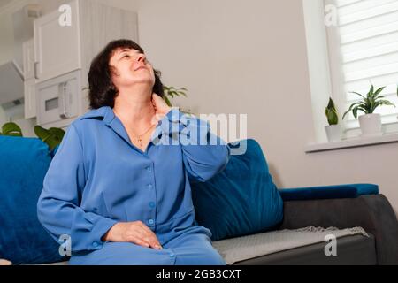 Ältere Frau im blauen Hemd, die unter Nackenschmerzen leidet Stockfoto