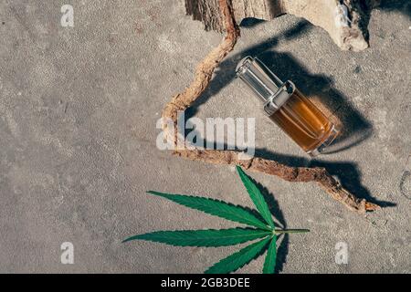 Glasflasche mit CBD-Öl, THC-Tinktur und Hanfblatt auf grauem Marmorboden. Minimalismus, Natürlichkeit. CBD-Öl-Kosmetik. Stockfoto