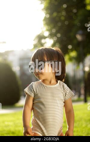 Kleiner 1-jähriger lateinischer Junge im Park bei Sonnenuntergang mit der Sonnenbrille seines Vaters Stockfoto