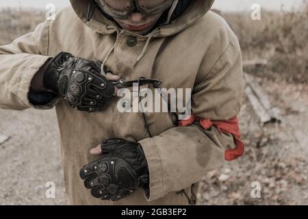 Wandernder Junge. Junge mit einer Waffe. Junge geht zu einem verlassenen Gebäude. Junge steht vor einem Gebäude. Post-Apokalypse. Mann, der zu Fuß in einem Stockfoto