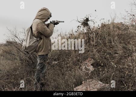 Wandernder Junge. Junge mit einer Waffe. Junge geht zu einem verlassenen Gebäude. Junge steht vor einem Gebäude. Post-Apokalypse. Mann, der zu Fuß in einem Stockfoto