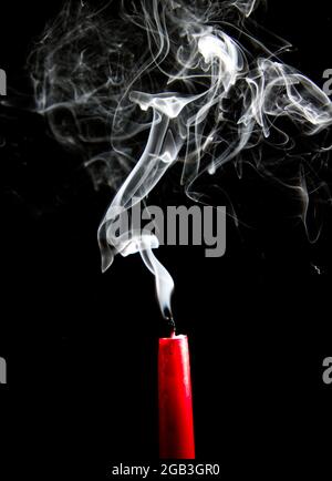 Rauch steigt aus einer erloschenen roten Kerze auf schwarzem Hintergrund Stockfoto