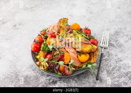 Omelette mit geschmortem Gemüse und Lachs, Tomaten mit Zwiebeln, Brokkoli und rotem Fisch mit Erbsen-Microgreens, leckeres herzhaftes Frühstück Stockfoto