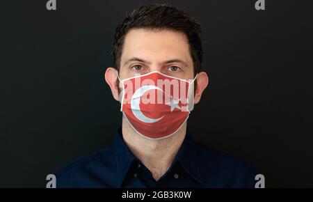 Mann mit türkischer Flagge schützende medizinische Gesichtsmaske. Er sieht besorgt und besorgt aus. Coronavirus-Konzept in der Türkei mit schwarzem Hintergrund. Stockfoto
