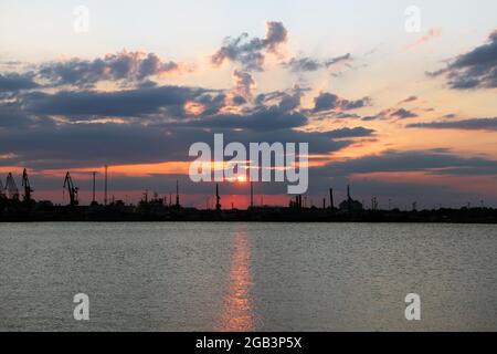 Wunderschöne Landschaft Hafen von Tallinn bei Sonnenaufgang. Kräne Silhouetten gegen feurigen, orangen und roten Himmel. Seaport Silhouetten und rote Sonne Stockfoto