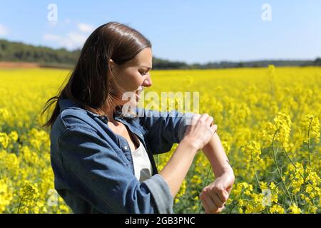 Gestresste Frau kratzt Arm in einem Feld im Sommer Stockfoto