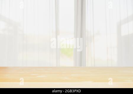 Leere Holztischplatte mit unverschämtem Vorhangfenster mit Blick auf den Garten in der Sommersaison. Hintergrundnutzung und Platz für Ihre Produktpräsentation. Stockfoto