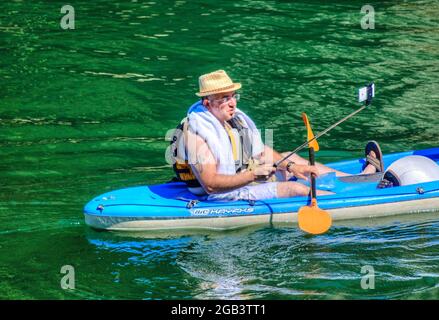 Ein Mann macht ein Foto von sich selbst, wie er mit einem Kajak über den See rudert. Stockfoto