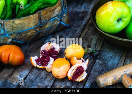 Die Maracuya-Frucht öffnete sich in zwei Hälften und zeigte ihre roten Samen auf einem Holztisch mit Tomaten, Äpfeln und einem Korb mit Paprika Stockfoto