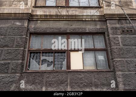 Großes schmutziges kaputtes Fenster. Dunkle Wand eines großen Hauses. Vintage-Architektur, klassische Fassade, altes graues Gebäude, Vorderansicht Stockfoto