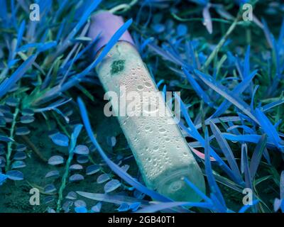 Kosmetikflasche auf Grasfeld liegend, Naturverschmutzungskonzept mit Kunststoffgegenstand. Stockfoto