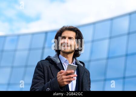 Moderne selbstbewusste junge Geschäftsmann in Vollanzug steht im Freien mit Stadtbild im Hintergrund Stockfoto
