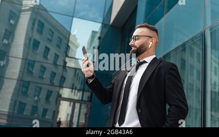 Reifer Unternehmer Mann, der Musik in drahtlosen Kopfhörern hört und im Freien auf dem Smartphone im Internet surft Stockfoto