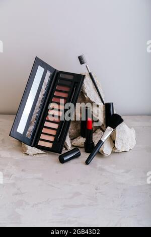 Dekorative Kosmetik für Make-up auf Steinsockel. Rote scharlachrote Lippenstift-Lidschatten-Make-up-Pinsel auf grauem Beton-Hintergrund. Minimale Ästhetik Stockfoto