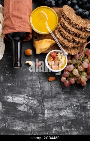 Mediterrane Speisen Getränke Zutaten für das Abendessen. Wein Honig Käse Nüsse Snacks Brot Trauben Obst auf dunklem schwarzem Stein Hintergrund mit Kopierraum Stockfoto