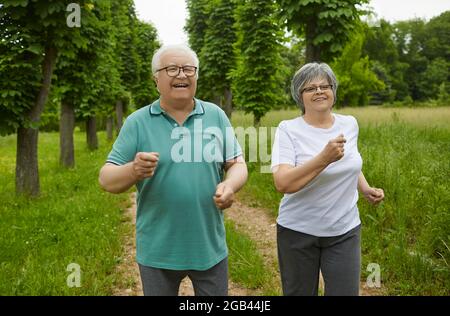 Lächelndes, aktives Senior-Paar in Sportswear joggt gemeinsam im grünen Park Stockfoto