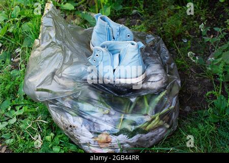 Paar alte schmutzige blaue Sneakers in schwarzem Müllbeutel auf grünem Gras Hintergrund Stockfoto