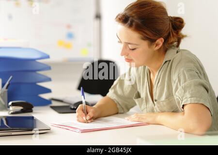 Entspannte Frau, die am Schreibtisch im Büro Papier ausfüllt Stockfoto