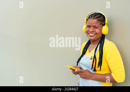 Afroamerikanische Frau, die Musik hört und ein Smartphone benutzt, während sie auf einem grauen Hintergrund steht. Stockfoto