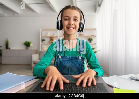 Mädchen, das am Schreibtisch sitzt, einen Laptop benutzt, ein Headset trägt, tippt Stockfoto