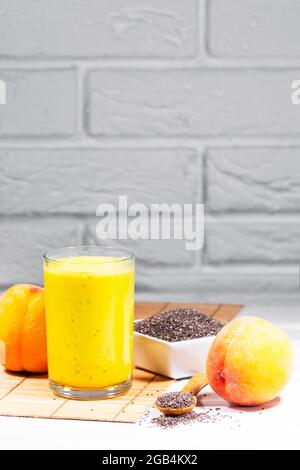 Stillleben mit Frucht-Smoothie, Pfirsich- und Chiasamen auf weißem Backstein-Hintergrund, vertikaler Auflösung, gesunder Sommerdiät Stockfoto