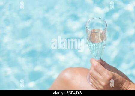 Hand des weiblichen Modells hält ein Glas Champagner. Die Poolebene befindet sich im Hintergrund. Stockfoto