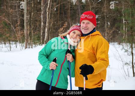 Senior Paar Walking mit nordic Walking Stöcken im verschneiten Winter Wald Stockfoto