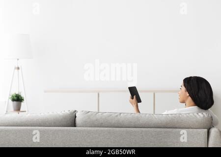 Glückliche afroamerikanische Dame, die die Heiztemperatur des Hauses mit dem Handy kontrolliert, Platz auf der weißen Wand kopieren Stockfoto