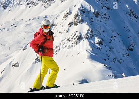 Skifahrerin mit medizinischer Maske und farbenfroher Kleidung im Skigebiet Arosa Lenzerheide, an einem sonnigen Wintertag. Schweiz Winteraktivitäten. Stockfoto