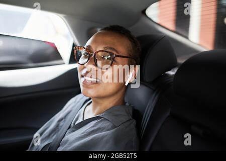 Porträt einer afrikanischen Geschäftsfrau in einer Brille, die auf dem Rücksitz des Autos sitzt und die Kamera anlächelt Stockfoto