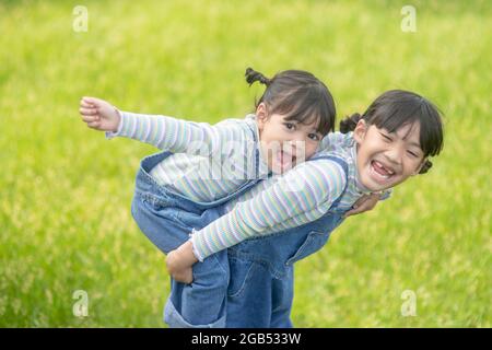 Asiatisches kleines Mädchen mit älterer Schwester in einem Park, der auf ihrem Rücken reitet Stockfoto