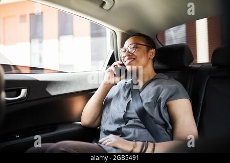 Glückliche Afrikanerin, die im Auto sitzt und während ihres Gesprächs auf dem Handy lächelt Stockfoto