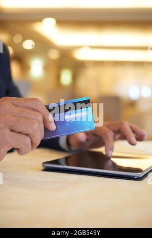 Hände eines Geschäftsmannes, der mit Kreditkarte für Einkäufe bezahlt, die er online über eine Anwendung auf einem Tablet-Computer getätigt hat Stockfoto