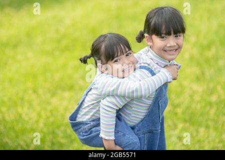 Asiatisches kleines Mädchen mit älterer Schwester in einem Park, der auf ihrem Rücken reitet Stockfoto