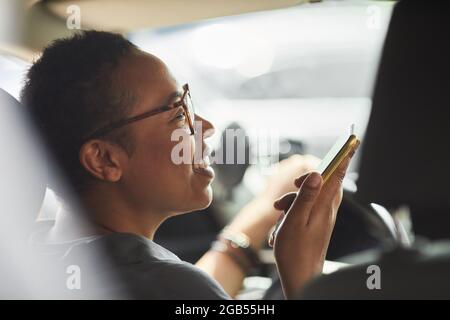 Nahaufnahme einer jungen afrikanischen Frau, die am Mobiltelefon spricht und lächelt, während sie am Auto vorbei fährt Stockfoto