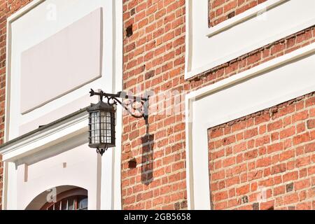 Die Lampe, stilisiert wie eine alte, hängt an einer Backsteinmauer eines historischen Gebäudes. Sommer. Stockfoto