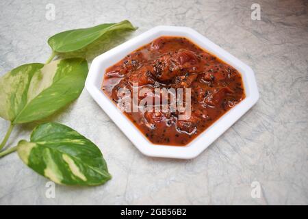 Pflaumenchutney süßes und würziges indisches Chutney mit wenig Gewürzen aus gehärtetem Tadka auf weißem Hintergrund, dekpriert mit Geldpflanze und Hibiskusrot Stockfoto