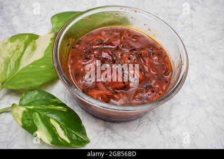 Pflaumenchutney süßes und würziges indisches Chutney mit wenig Gewürzen aus gehärtetem Tadka auf weißem Hintergrund, dekpriert mit Geldpflanze und Hibiskusrot Stockfoto