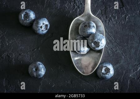 Frische süße Heidelbeer-Beeren im silbernen Löffel auf schwarzem Hintergrund. Food-Fotografie Stockfoto