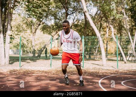 Afroamerikanischer Basketballspieler auf einem Sportplatz im Freien, der mit einem Ball spielt. Sport auf der Straße. Stockfoto