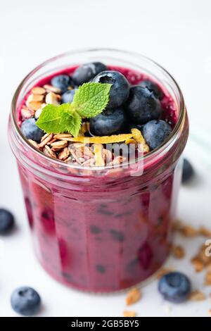 Lila Acai Blueberry Smoothie In Glas Mit Granola Und Heidelbeeren Auf Weißem Hintergrund Gekrönt Stockfoto