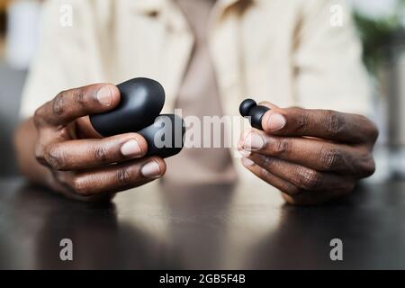Nahaufnahme eines afrikanischen Mannes, der am Tisch sitzt und den Koffer mit kabellosen Kopfhörern öffnet Stockfoto