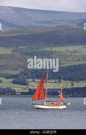 Menai Strait, Landschaft von Wales; ein Ketchboot, das entlang der Menai Strait zwischen Anglesey und dem Festland von Wales fährt, von Anglesey aus gesehen, Wales, Großbritannien Stockfoto