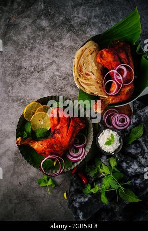 Hausgemachte Tandoori-Hähnchenschenkelstücke, serviert auf einem Teller mit Roti Paratha und Reis – indisches Speisekonzept Stockfoto